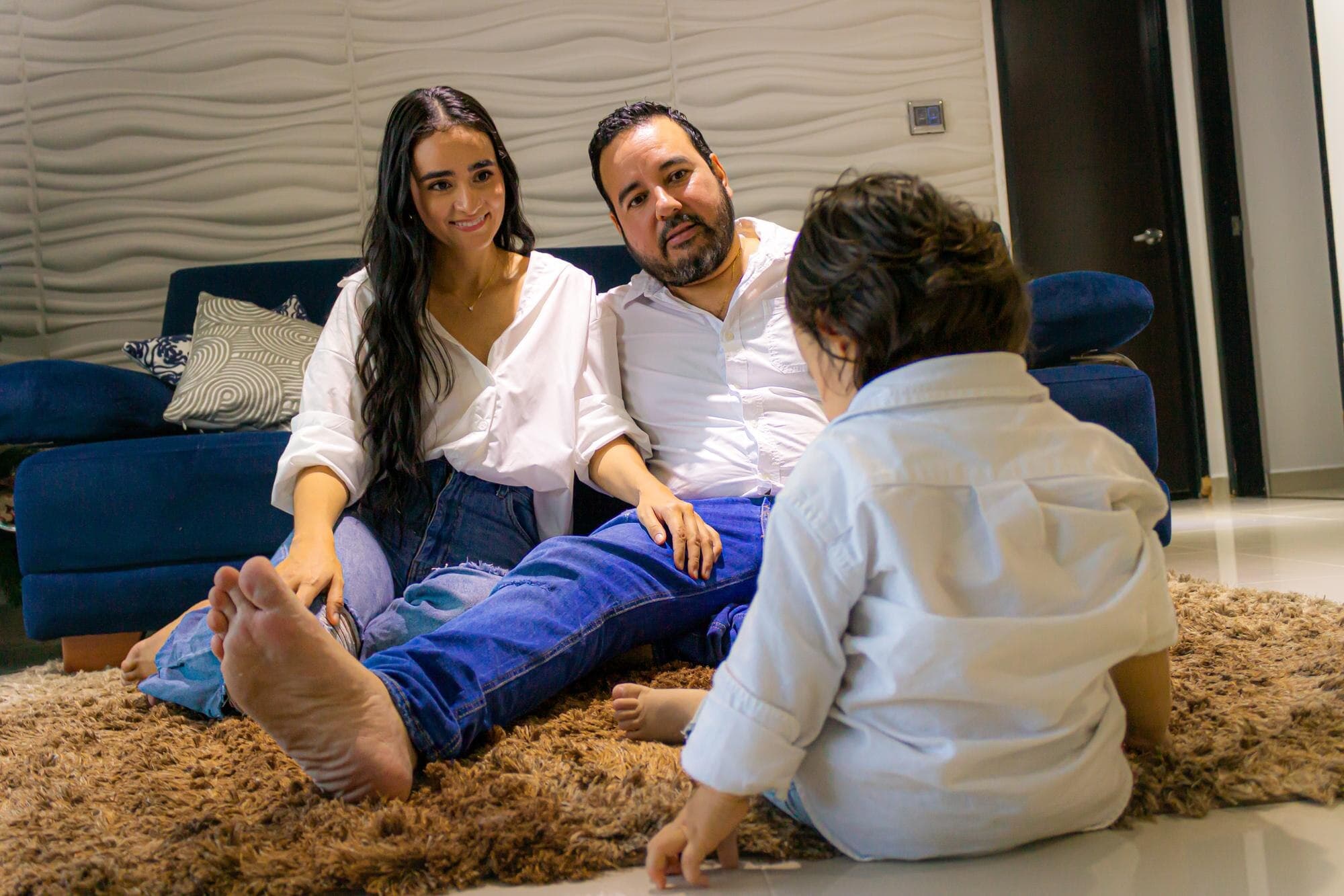 Padres latinos mirando con cariño a su hijo en la sala de estar